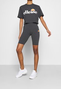 Grå kortärmad t-shirt med "ellesse"-logotyp i vitt och orange, ihop med grå cykelbyxor med en liten logotyp. Bärs med vita sneakers.
