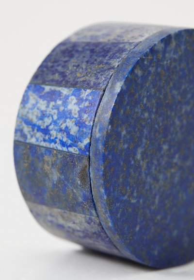 Blå dekorativt föremål med cylindrisk form, med variationer i textur och nyans, inklusive streck och fläckar av ljusare blått och guld.