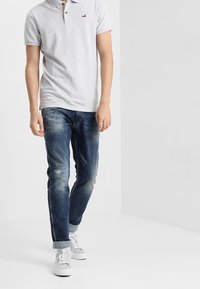 Šedá polokošile s krátkým rukávem a límečkem, modré oprané džíny a bílé tenisky. Tento outfit má neformální styl.