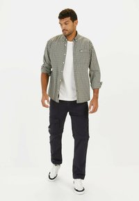 Geverfde zwart-witte button-up shirt over een wit T-shirt, gecombineerd met donkere cargo-broeken. De outfit wordt compleet gemaakt met sneakers met zwart-witte accenten.