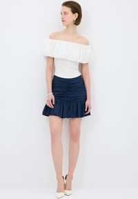 Top bianco scollato con dettagli arricciati abbinato a una mini gonna blu scuro con texture, dotata di orlo svasato e design arricciato.