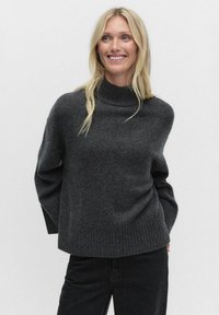 Donkergrijze trui met een hoge hals, geribde onderrand en manchetten. Gemaakt van zacht materiaal; heeft een losse pasvorm en lange mouwen.