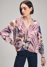Blouse à motifs floraux en rose, avec des détails volantés le long de l'encolure et des manches, à manches longues et à décolleté en V.
