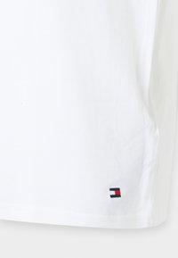 Tissu blanc avec un petit logo rectangulaire comportant des bandes bleu marine, blanc et rouge près du coin inférieur droit.