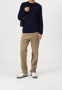 Marineblauwe, gebreide trui met lange mouwen, kaki corduroy broek, witte sneakers met zwarte strepen, en een kleine zwarte schoudertas.