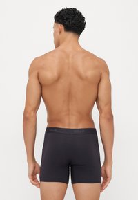 Zwarte boxershorts gemaakt van een rekbaar materiaal, met een effen kleur en een merklogo op de band aan de achterkant. De pasvorm is snug met een midden-hoge pasvorm.