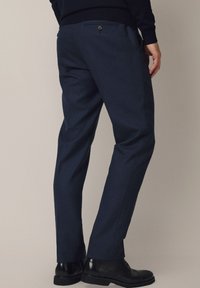 Granatowe spodnie wizytowe o prostym kroju, gładkiej fakturze i subtelnym połysku. Posiadają pojedynczą kieszeń z tyłu oraz zapięcie na guzik.