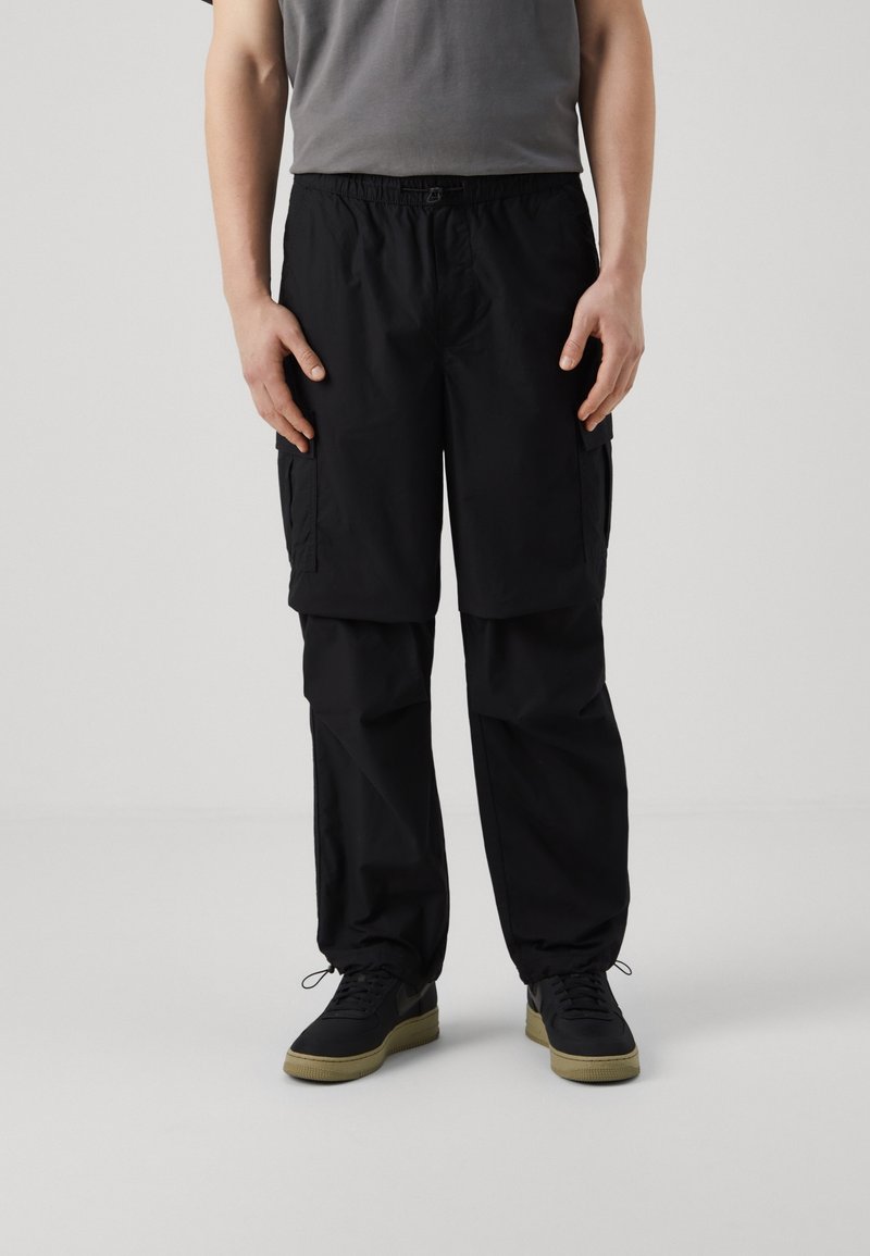 Czarne spodnie cargo z elastycznym pasem, bocznymi kieszeniami i luźnym krojem; wykonane z lekkiego materiału o gładkiej fakturze.