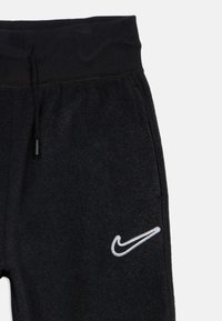 Čierne tepláky s rebrovaným pásom, sťahovacím šnúrkovým uzáverom, bočnými vreckami a bielou vyšitou logom Nike na ľavom stehne.