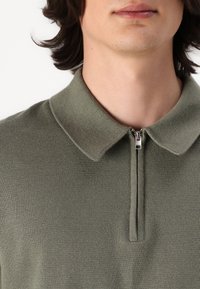 Grünes gestricktes Poloshirt mit Reißverschlusskragen und kurzen Ärmeln, das eine glatte Textur und eine lässige Passform bietet.