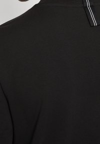 Camiseta negra con un tejido texturizado y suave, que presenta un acento de rayas verticales contrastantes en la parte posterior del cuello.
