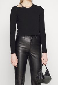 Haut noir à rayures à manches longues avec un détail d'encolure asymétrique, associé à un pantalon en cuir noir taille haute et un petit sac à main texturé.