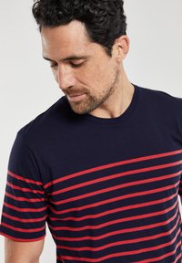 Marineblå crewneck t-shirt med vandrette røde striber. Lavet af stof med en glat tekstur. Korte ærmer, afslappet design.