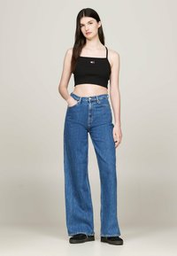 Top corto nero a coste con spalline sottili abbinato a jeans in denim blu a vita alta e gamba larga. I jeans presentano tasche frontali e chiusura con bottone.