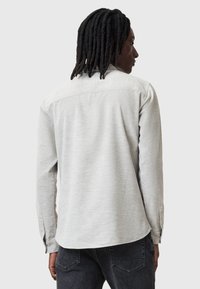 Lys grå langærmet skjorte med tekstureret stof, knapmanchetter og en buet bund. Har et rygdesign med yoke.
