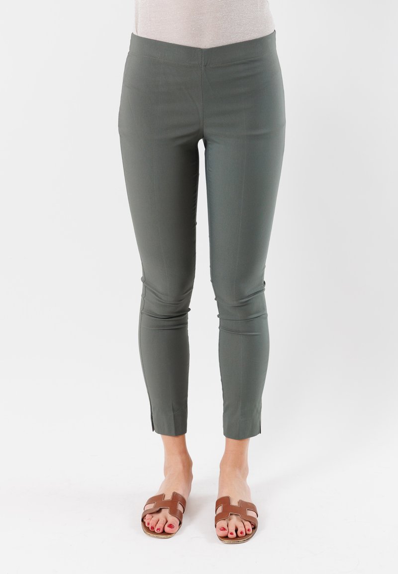 Pantaloni verdi aderenti con una texture liscia, lunghezza cropped e fessure laterali; abbinati a sandali a scivolo marroni.