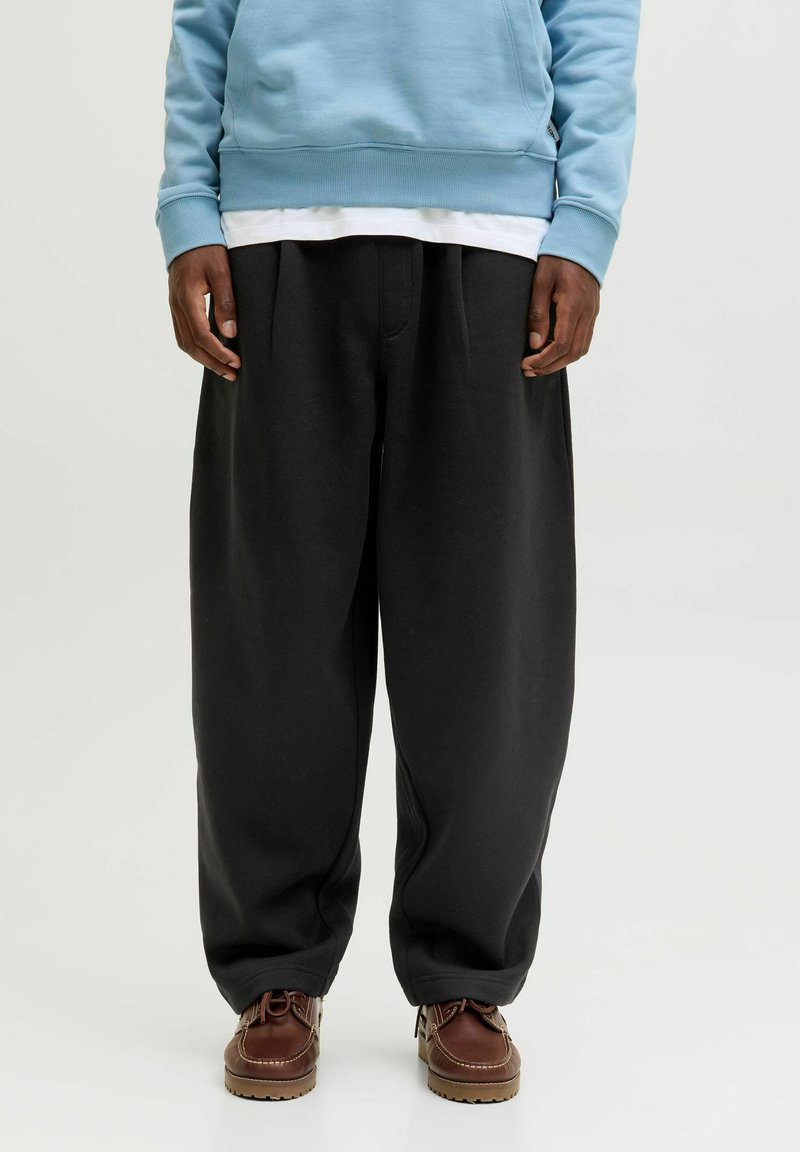 Sorte sweatpants med løs pasform og plisseret front, parret med en lyseblå hættetrøje. Brune sko med kontraststing bæres.