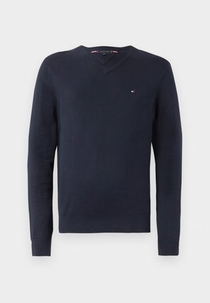 Marineblauw V-halstrui gemaakt van zacht materiaal met lange mouwen. Beschikt over een klein logo op de borst en ribgebreide manchetten en zoom.