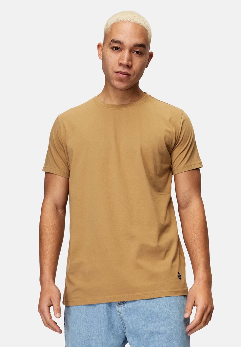 Brun bomulds t-shirt med rund halsudskæring, korte ærmer og et diskret brandlogo-label i kanten. Glat struktur, afslappet pasform.