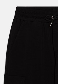 Schwarze Jogginghose mit elastischem Taillenbund und Kordelzug, seitlichen Taschen und weicher Textur. Enthält eine aufgesetzte Tasche am Bein.