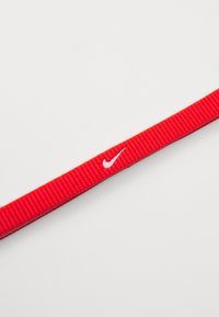 Cinghia in nylon rosso con texture rigata, adornata da un piccolo logo Nike bianco. La cinghia è piatta e di forma continua.