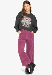 Black cropped sweatshirt featuring graphic print on the front, paired with high-waisted, wide-leg purple corduroy pants and black ankle boots.