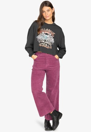 Black cropped sweatshirt featuring graphic print on the front, paired with high-waisted, wide-leg purple corduroy pants and black ankle boots.