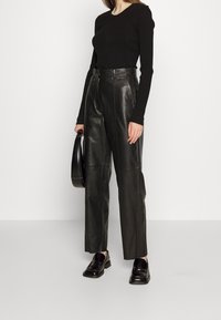 Pantaloni neri in pelle a vita alta con una texture liscia, caratterizzati da una vestibilità sartoriale e gambe dritte, abbinati a un top aderente nero a maniche lunghe.