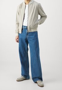 Světle šedá bomber bunda se zipem, bílý tričko a široké modré džínové kalhoty. Měkká textura a uvolněný střih s minimálními detaily.