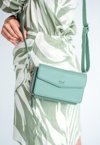 Mint green crossbody bag with a flap closure, silver hardware, zippered compartment, and textured surface. Features an adjustable strap.