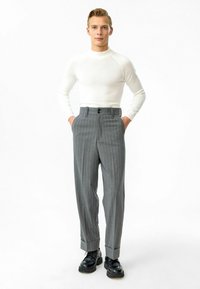 Grijze broek met fijne strepen, hoge taille en omgeslagen broekspijpen, gecombineerd met een aansluitend wit overhemd met lange mouwen. Zwarte veterschoenen.