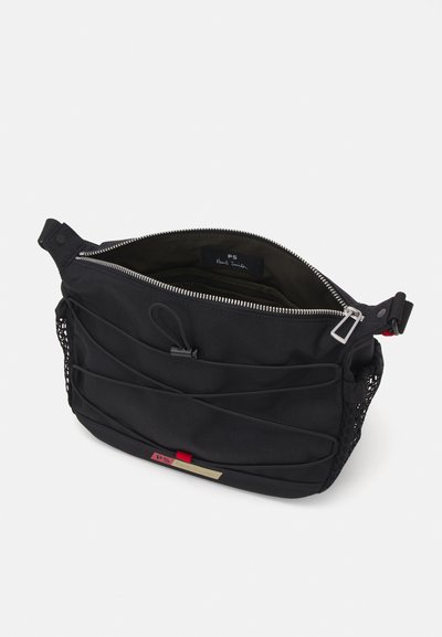 Borsa a spalla in tessuto nero con chiusura a zip, esterno testurizzato, pannelli laterali in rete e un'etichetta di accento rossa. L'interno presenta una fodera scura.