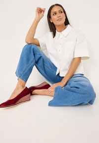 Červené lakované wedges s pletenou texturou na podpatku, spárované se svetle modrými širokými džíny a bílou košilí s krátkým rukávem na knoflíky.