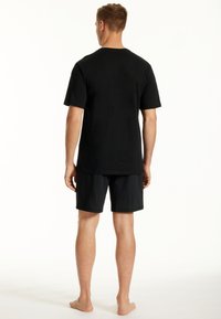Schwarzes Baumwoll-T-Shirt mit Rundhalsausschnitt, kombiniert mit schwarzen Mesh-Shorts, beide mit lockerer Passform und minimalistischem Design.