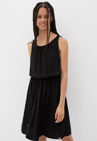 Schwarzes ärmelloses Kleid mit gerafftem Ausschnitt, lockerer Passform und elastischem Bund. Weicher Stoff mit einem fließenden Rock und subtiler Glanz.