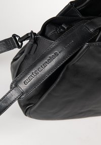 Zwarte leren schoudertas met gegraveerd "aunts & uncles" logo op de riem, voorzien van metalen sluitingen en verstelbare details.
