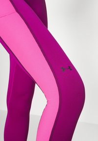 Leggings aderenti in un vivace viola e rosa, con texture a coste, strisce laterali a contrasto e un piccolo accento di logo nero.