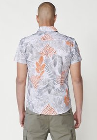Camicia a maniche corte di colore bianco con un motivo a foglia tropicale grigio e arancione. Realizzata in materiale leggero, presenta un colletto a punta e un orlo curvo.