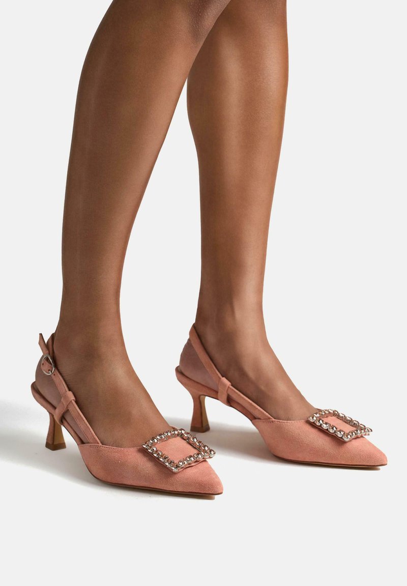 Pink suede slingback heels with a pointed toe, embellished with a diamond-shaped rhinestone buckle, and a chunky heel.