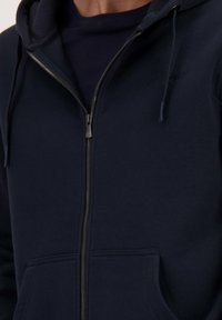 Navy zip-up hoodie van een zachte katoenmix, met een voorzak, een capuchon met koord en een subtiele logo-detail op de borst.