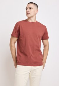 Czerwona bawełniana koszulka z okrągłym dekoltem i krótkimi rękawami. Posiada gładką teksturę i klasyczny krój, zaprezentowana na jednolitym tle.