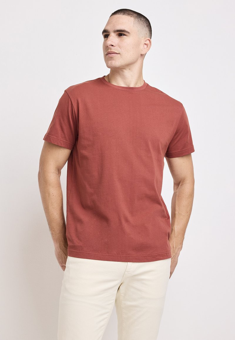 Czerwona bawełniana koszulka z okrągłym dekoltem i krótkimi rękawami. Posiada gładką teksturę i klasyczny krój, zaprezentowana na jednolitym tle.