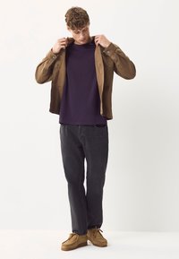 Brun jakke over en lilla t-shirt, kombineret med mørke jeans og tanfarvede sko. Jakken har knapper og en afslappet pasform.