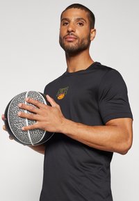 Svart treningsskjorte med en gul Nike-logo; holder en mønstret svart og grå basketball med hvite striper; nærbilde.