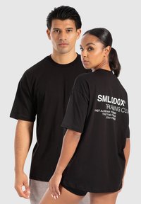 Sorte bomulds t-shirts med korte ærmer, der har hvid tekst på ryggen med teksten "SMILODOX TRAINING CLUB." Klassisk pasform og rund halsudskæring.