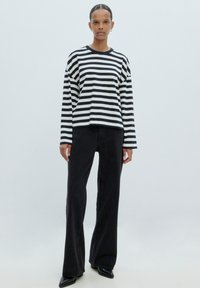 Zwart-wit gestreepte langemouwen shirt gecombineerd met hoge taille zwarte flared jeans, met een ontspannen pasvorm en een zachte textuur.