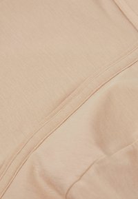 Light peach fabric with a soft texture, featuring smooth seams and a slightly wrinkled appearance, indicating stretch and flexibility.