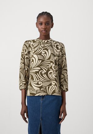 Olive green top with cream swirling patterns, round neckline, and three-quarter sleeves; paired with a denim skirt featuring a front slit.