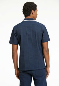 Camisa de manga corta en color navy con tejido texturizado, presenta rayas verticales y un cuello en contraste. Ajuste relajado, combinada con pantalones a juego.