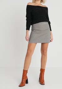 Schwarzer schulterfreier Pullover mit geripptem Design, kombiniert mit einem karierten Minirock und glänzenden braunen Blockabsatz-Stiefeletten.